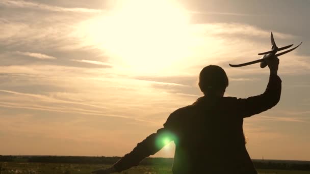 Дети на фоне солнца с самолетом в руке. Девушка играет с игрушечным самолетом на закате. Мечтает летать. Счастливое детство. Силуэт детей, играющих в самолете — стоковое видео