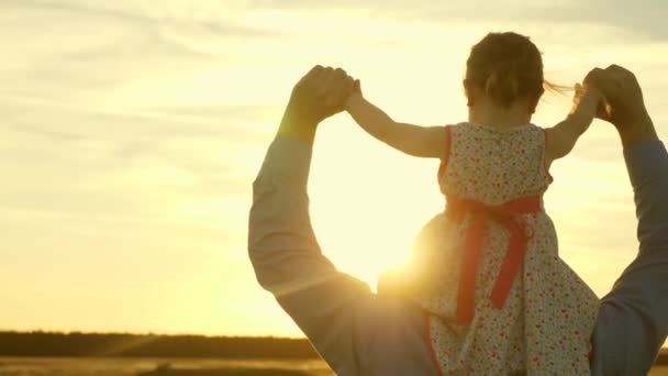 Papa dansen op zijn schouders met zijn dochter in de zon. Vader reist met baby op zijn schouders in stralen van zonsondergang. Een kind met ouders loopt bij zonsondergang. gelukkige familie rusten in Park. familieconcept — Stockvideo