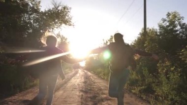 çocuk gezginler. Yürüyüşçü Kız. sırt çantaları ile mutlu kız gezginler parlak güneşin ışınları el ele tutarak ülke yol boyunca çalıştırın. spor turizmi ve seyahat kavramı. genç kızlar seyahat ve tutun