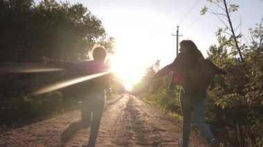 genç kızlar seyahat ve el ele tutuşur. çocuk gezginler. Yürüyüşçü Kız. sırt çantaları ile mutlu kız gezginler parlak güneşin ışınları el ele tutarak ülke yol boyunca çalıştırın. spor turizmi kavramı ve