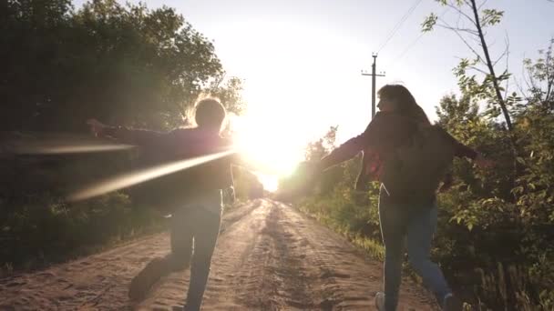 Adolescentes viajan y se toman de la mano. niños viajeros. Hiker Girl. niñas felices viajeros con mochilas corren a lo largo de carretera del país tomados de la mano en los rayos del sol brillante. concepto de turismo deportivo y — Vídeo de stock