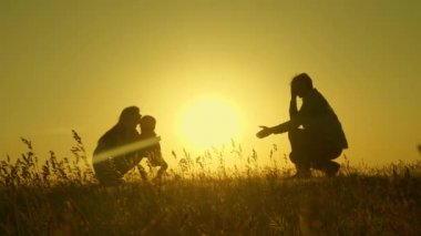 Ailesi gün batımında atlayan küçük bir kız. Anne baba ve bebeğin siluetleri şafak ışınlarında. Aile konsepti. Doğada küçük bir çocukla yürümek.