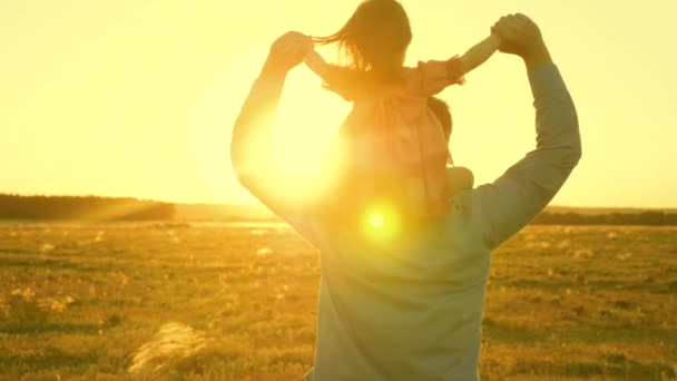 Tata tańczy na ramionach z córką w słońcu. Ojciec podróżuje z dzieckiem na ramionach w promieniach zachodu słońca. Dziecko z rodzicami idzie o zachodzie słońca. Szczęśliwego rodzinnego odpoczynku w parku. koncepcja rodzinna — Wideo stockowe