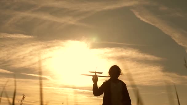 Marzenia o lataniu. Dzieci na tle słońca z samolotu w ręku. Sylwetka dzieci bawią się na płaszczyźnie. dziewczyna grać z samolotem zabawka o zachodzie słońca. Szczęśliwa koncepcja dzieciństwa. — Wideo stockowe