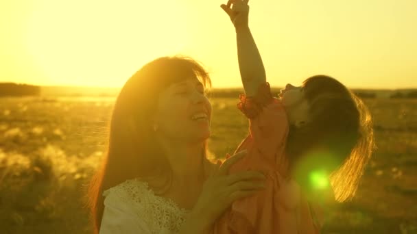 Szczęśliwa matka idzie z córką w ramiona w promieniach zachodu słońca. Mama rozmawia z szczęśliwym dzieckiem, dziecko siedzi na ramionach matek o zachodzie słońca Złotego słońca. Zwolnionym. — Wideo stockowe