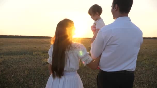 Rodzina gra z dzieckiem o zachodzie słońca. Tata i Mama chodzą z córką w ramionach o zachodzie słońca. ojciec z córkami spoczywających w parku. koncepcja szczęśliwej rodziny i dzieciństwa. — Wideo stockowe