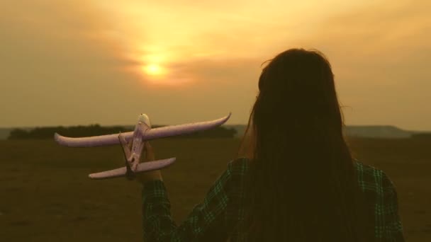 Niños juegan juguete avión. Las chicas sueñan con volar y convertirse en piloto. En cámara lenta. Hermanas chicas felices corren con un avión de juguete al atardecer en el campo. El concepto de una familia feliz . — Vídeo de stock