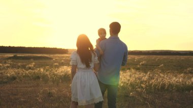 Aile gün ışığında kızları ile oynuyor. mutlu çocuk ebeveynlerin elinde oturan. Anne ve baba gün batımında parkta küçük kızları ile oynarlar. parkta bebek ile aile yürüyüşü.