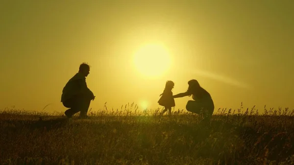 Mamá y papá juegan con su hija pequeña. niño feliz va de padre a madre. Mamá y papá juegan con su hija al sol. familia joven con un hijo de 1 año. concepto de felicidad familiar . — Foto de Stock