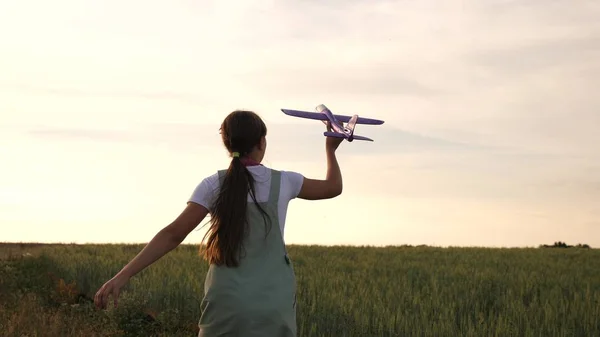 Lycklig tjej springer med en leksaks plan på ett vetefält. barn leker leksaksflygplan. tonåring drömmer om att flyga och bli en pilot. flickan vill bli pilot och astronaut. — Stockfoto