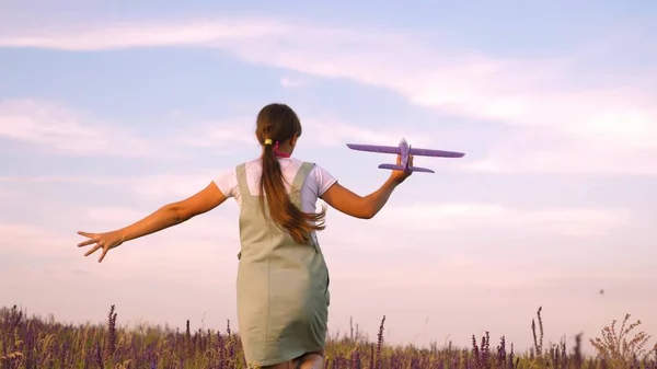 Lycklig flicka går med en leksak flygplan på en blomma fält. barn leker leksaksflygplan. tonåring drömmer om att flyga och bli en pilot. flickan vill bli pilot och astronaut. — Stockfoto