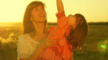 mutlu anne gün batımı ışınlarında kollarında kızı ile yürür. Anne mutlu bebek ile konuşuyor, bebek altın güneşin gün batımında annelerin kollarında oturuyor. Yavaş çekim.