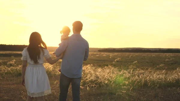 Famiglia che gioca con la figlia sotto il sole. bambino felice seduto sulle mani dei genitori. Mamma e papa 'giocano con la loro figlioletta al parco al tramonto. passeggiata in famiglia con il bambino nel parco . — Foto Stock