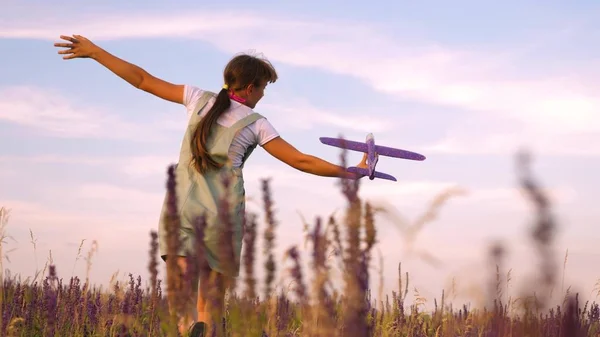 Ragazza felice corre con un aeroplano giocattolo su un campo di fiori. i bambini giocano aereo giocattolo. adolescente sogna di volare e diventare un pilota. la ragazza vuole diventare un pilota e astronauta . — Foto Stock