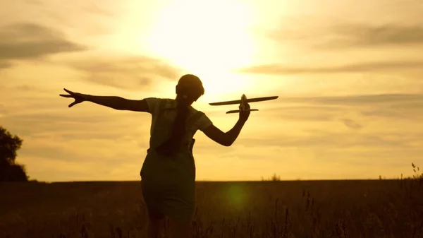 Chica joven corre con un avión de juguete en el campo en los rayos de cilicio. niños juegan juguete avión. adolescente sueña con volar y convertirse en piloto. la chica quiere convertirse en piloto y astronauta . —  Fotos de Stock