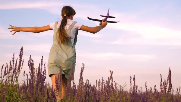 Menina feliz corre com um avião de brinquedo em um campo de flores. As crianças brincam de avião de brinquedo. adolescente sonha em voar e se tornar um piloto. a menina quer se tornar um piloto e astronauta . — Fotografia de Stock