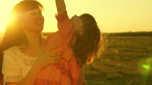 Mère heureuse marche avec sa fille dans ses bras dans les rayons du coucher du soleil. Maman parle avec bébé heureux, bébé est assis sur les bras des mères au coucher du soleil doré. Mouvement lent . — Photo