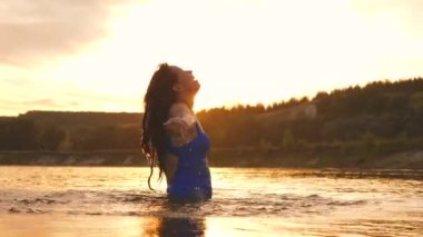 neşeli kız ferahlatıcı bir nehir suyu ile tropikal adanın yakınında ferahlatıcı bir yaz akşamı onu uzun saçları sıçraması. Kız geri saç çevirir. gün batımı ışınları su güzel sprey. su sıçrama