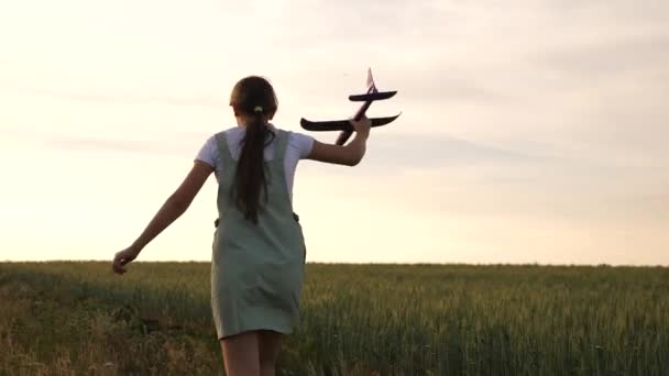 Ευτυχισμένο κορίτσι τρέχει με ένα αεροπλάνο παιχνίδι σε ένα χωράφι λουλουδιών. παιδιά παίζουν παιχνίδι αεροπλάνο. Έφηβος ονειρεύεται να πετάξει και να γίνει πιλότος. το κορίτσι θέλει να γίνει πιλότος και αστροναύτης. — Αρχείο Βίντεο