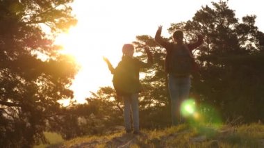 kızlar bir kır yolda sırt çantaları ile seyahat. Yürüyüşçü Kız. Iki kız seyahat, ormanda yürümek ve tepede ellerini sallamak. Tatil seyahatlerinde mutlu bir aile. spor turizmi konsepti.