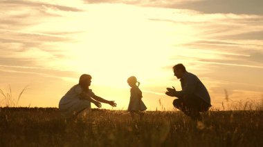 Annem ve babam gün batımında parkta kızlarıyla oynuyor. Çocuk ilk adımları alır. Mutlu aile güneş ışınları çocuk ile oynuyor. Bebek babasından anneme gider ve gülüyor. Yavaş hareket.