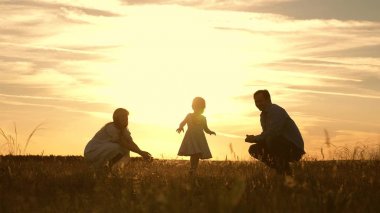 Annem ve babam gün batımında parkta kızlarıyla oynuyor. Çocuk ilk adımları alır. Mutlu aile güneş ışınları çocuk ile oynuyor. Bebek babasından anneme gider ve gülüyor. Yavaş hareket.