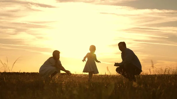 Máma s tátou si hráli se svou dcerou v parku při západu slunce. dítě dělá první kroky. Šťastná rodina si hraje s dítětem v paprscích slunce. dítě chodí od táty k mamince a směje se. Zpomaleně. — Stock fotografie