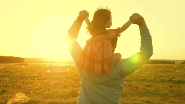 Papà danzava sulle spalle con sua figlia al sole. Papà viaggia con il bambino sulle spalle in raggi di tramonto. Un bambino con i genitori cammina al tramonto. famiglia felice che riposa nel parco. concetto di famiglia — Foto Stock