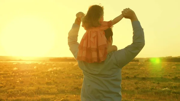 O pai a dançar nos ombros com a filha ao sol. Pai viaja com bebê em seus ombros em raios de pôr do sol. Uma criança com pais caminha ao pôr do sol. família feliz descansando no parque. conceito de família — Fotografia de Stock