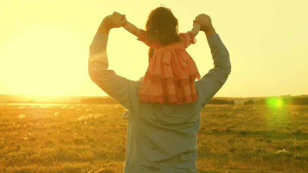 Папа танцует на плечах с дочерью на солнце. Отец путешествует с ребенком на плечах в лучах заката. Ребенок с родителями гуляет на закате. счастливая семья отдыхает в парке. семейная концепция — стоковое фото