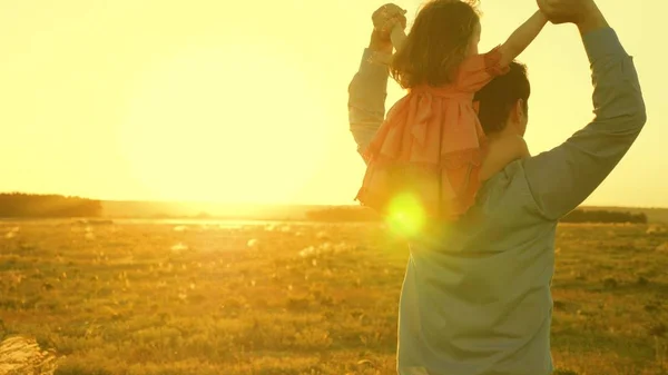 Papa dansen op zijn schouders met zijn dochter in de zon. Vader reist met baby op zijn schouders in stralen van zonsondergang. Een kind met ouders loopt bij zonsondergang. gelukkige familie rusten in Park. familieconcept — Stockfoto
