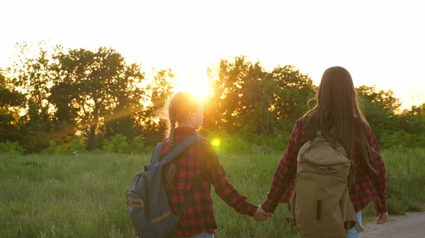 Turistické dívky na venkovské silnici. Hiker Girl, dívky cestují a drží se za ruce. dětské cestovatele. dívky s batohy jsou na venkovské silnici na slunci. koncepce sportovního turismu a cestování — Stock fotografie