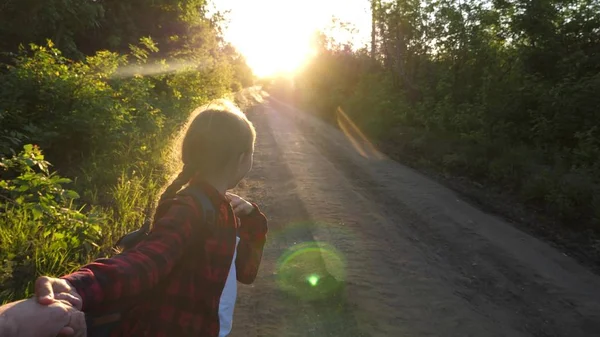 Ręce w miłości podróżują. Chodź ze mną. Hiker Girl z plecakiem trzyma człowieka ręką i prowadzi go. Młoda para trzyma ręce podróży na drodze wiejskiej w promieniach zachodu słońca. Praca w zespole turystów — Zdjęcie stockowe