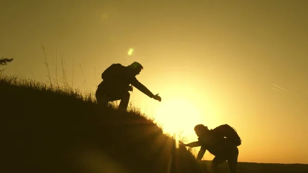 Los viajeros suben al acantilado cogidos de la mano. trabajo en equipo de gente de negocios. Feliz familia de vacaciones. hombre viajero extiende su mano a una chica que sube a la cima de una colina. turistas abrazo en la cima de la montaña —  Fotos de Stock