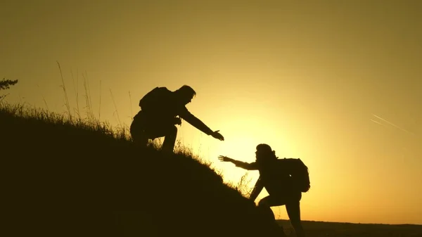 Os viajantes escalam o penhasco de mãos dadas. trabalho de equipa de pessoas de negócios. Família feliz de férias. homem viajante estende a mão para uma menina subindo para o topo de uma colina. turistas abraço no topo da montanha — Fotografia de Stock