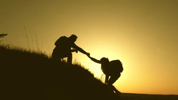 Los viajeros suben al acantilado cogidos de la mano. trabajo en equipo de gente de negocios. Feliz familia de vacaciones. hombre viajero extiende su mano a una chica que sube a la cima de una colina. turistas abrazo en la cima de la montaña —  Fotos de Stock