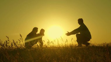 Ailesi gün batımında atlayan küçük bir kız. Anne baba ve bebeğin siluetleri şafak ışınlarında. Aile konsepti. Doğada küçük bir çocukla yürümek.