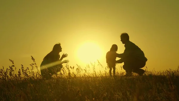 Little daughter with parents jumping at sunset. Silhouettes of mom dad and baby in the rays of dawn. Family concept. Walking with a small child in nature. — Stock Photo, Image