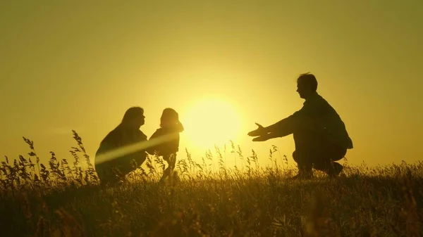 Hijita con padres saltando al atardecer. Siluetas de mamá papá y bebé en los rayos del amanecer. Concepto familiar. Caminar con un niño pequeño en la naturaleza . — Foto de Stock