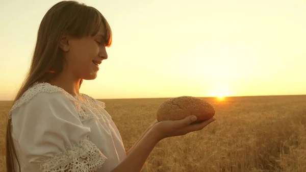 Pain dans les mains d'une jeune fille sur un champ de blé dans les rayons du coucher du soleil. savoureux pain sur les paumes. pain de seigle frais sur épis mûrs avec du grain. concept d'agriculture. produits de boulangerie — Photo