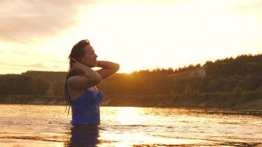 neşeli kız ferahlatıcı bir nehir suyu ile tropikal adanın yakınında ferahlatıcı bir yaz akşamı onu uzun saçları sıçraması. Kız geri saç çevirir. gün batımı ışınları su güzel sprey. su sıçrama