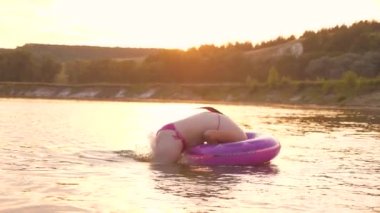 Bir mayo içinde güzel ve mutlu kız suda şişme bir daire içine dalış ve gülüyor. Sahilde yaz tatilleri. Sudaki oyunlar. Şehir dışında hafta sonu