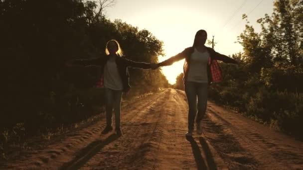 ハイカー・ガール子供の旅行者。十代の女の子が旅行し、手を握ります。バックパックを持つ幸せな女の子の旅行者は、明るい太陽の光の中で手をつないで田舎道に沿って実行されます。スポーツツーリズムの概念と — ストック動画