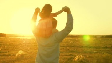 Babamın omuzlarında güneşte kızı ile dans ediyor. Baba gün batımı ışınları içinde omuzlarında bebek ile seyahat ediyor. Ebeveynleri olan bir çocuk gün batımında yürür. mutlu aile parkta istirahat. Aile konsepti