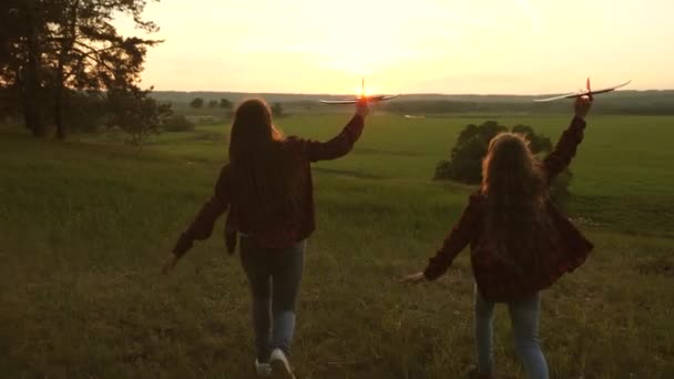 Sonhos de voar. Feliz conceito de infância. Duas raparigas brincam com um avião de brincar ao pôr-do-sol. Crianças no fundo do sol com um avião na mão. Silhueta de crianças brincando no avião — Vídeo de Stock