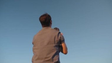 Baba kızını mavi gökyüzüne fırlatıyor. Babam kollarında gökyüzüne karşı küçük bir çocukla oynuyor. mutlu aile gökyüzüne karşı akşam oynarken. baba mutlu bebek, bebek gülümsüyor kusuyor