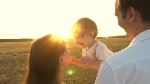 Pappa och mamma leker med en liten dotter i hennes armar vid solnedgången. familjevandringar med ett barn vid solnedgången. pappa leker med sina döttrar och vilar i parken. begreppet lycklig familj och barndom. — Stockvideo