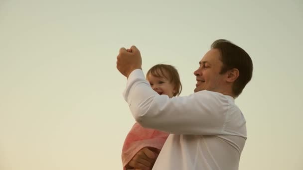 Papá bailando sobre sus hombros con su hija al sol. Padre viaja con el bebé sobre sus hombros en rayos de atardecer. Un niño con padres camina al atardecer. familia feliz descansando en el parque. concepto familiar — Vídeos de Stock