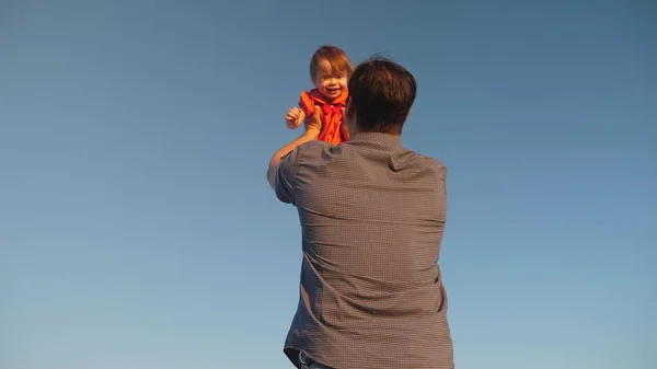 O pai atira a filha para o céu azul. O pai brinca com uma criança pequena. família feliz jogando à noite contra o céu. O pai vomita o bebé, o miúdo sorri. Movimento lento. família feliz — Fotografia de Stock