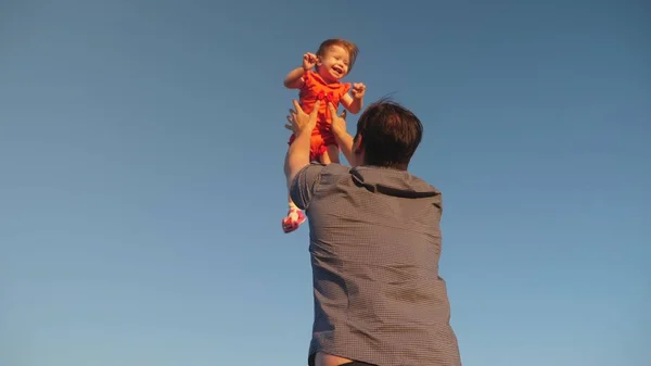 Dad throws up his daughter in the blue sky. Father plays with a small child. happy family playing in the evening against the sky. Dad throws up the baby, the kid smiles. Slow motion. happy family